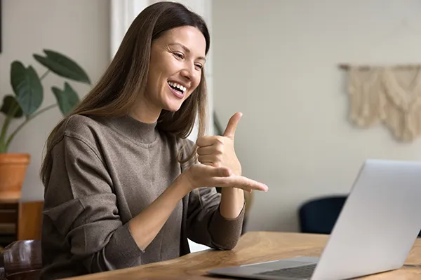 Happy communication expert speaking to patient with hearing disability online, showing thumb up on palm at computer, smiling, laughing.